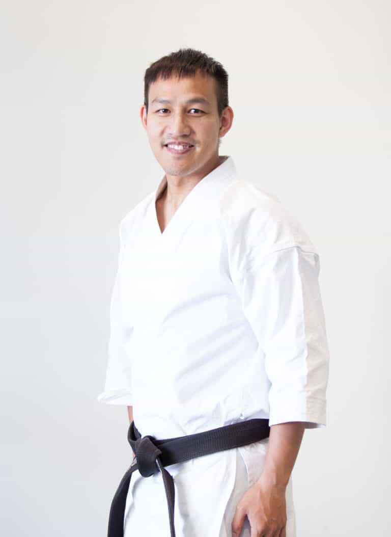 head and shoulder shot of a man in karate uniform and black belt smiling at the camera, Eric Truong