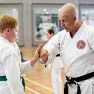 black belt man showing a young green belt how to punch and block correctly