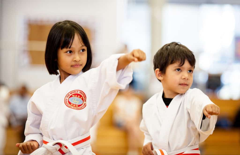 young boy and girl in a white karate uniform punching with left fist to the top right of the picture looking focused.