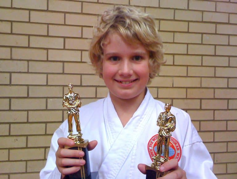 smiling young boy holding two first place competition trophies
