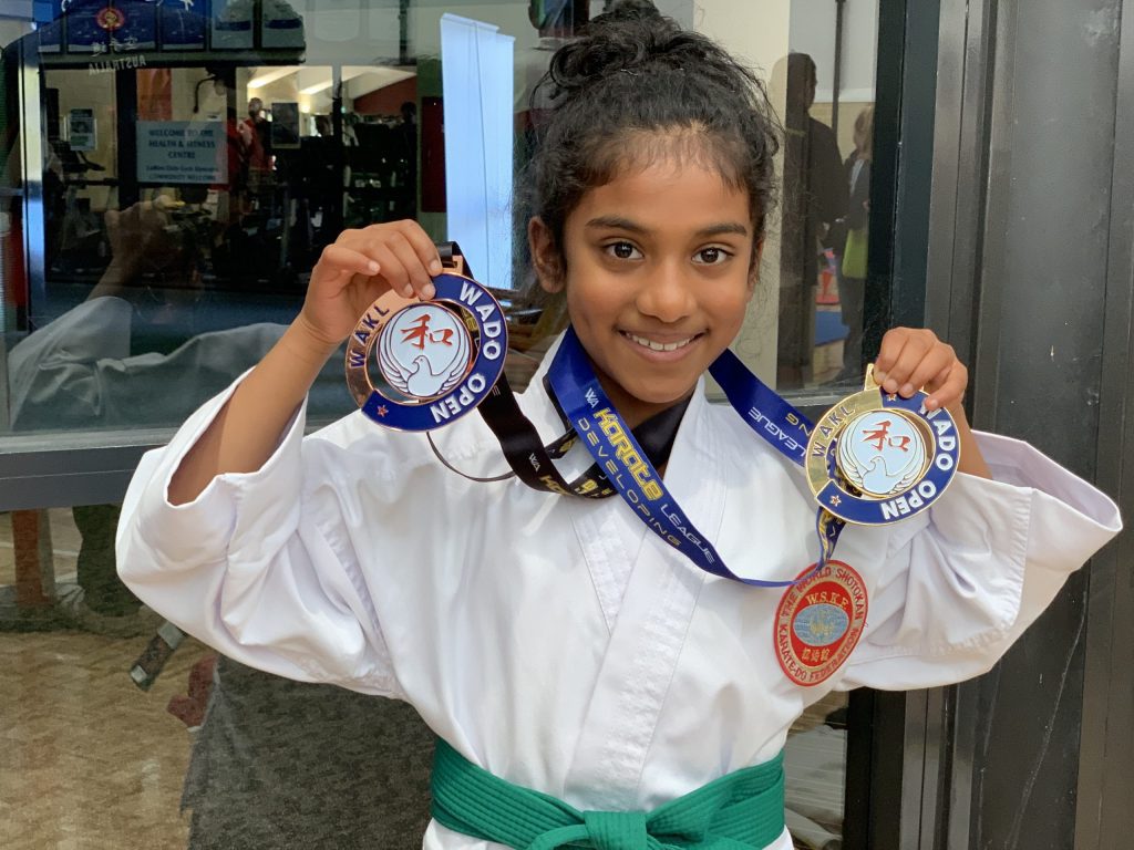 smiling young girl holding a first and third place completion medal